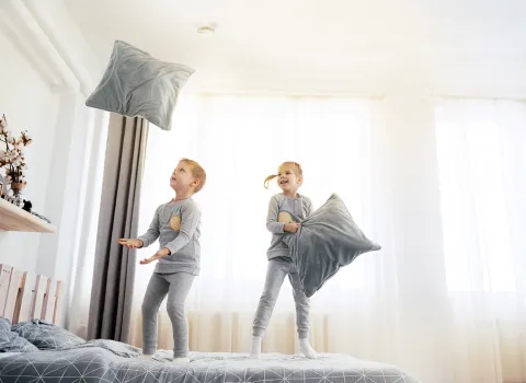 Kinder spielen mit Kissen auf einem Bett unter einem Rauchwarnmelder des Herstellers Hekatron Brandschutz.
