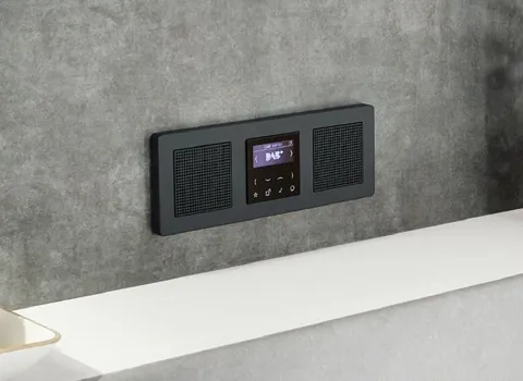 Digitales Unterputzradio mit Display und zwei integrierten Lautsprechern an einer grauen Wand, montiert oberhalb einer weißen Ablagefläche.